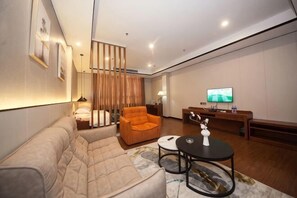 A modern living room with a sofa, armchair, coffee table, TV, and a desk with a chair. - Jiangmen Mintai Hotel (Jiangmen)