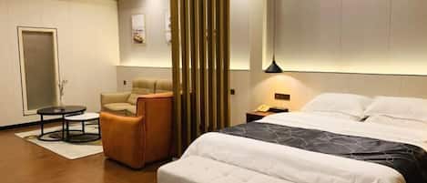 A modern hotel room with a large bed, a sofa, a small table, and a decorative partition.