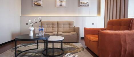 A modern living room with a sofa, two side tables, and a coffee table. There are framed pictures on the wall and a magazine on the floor.
