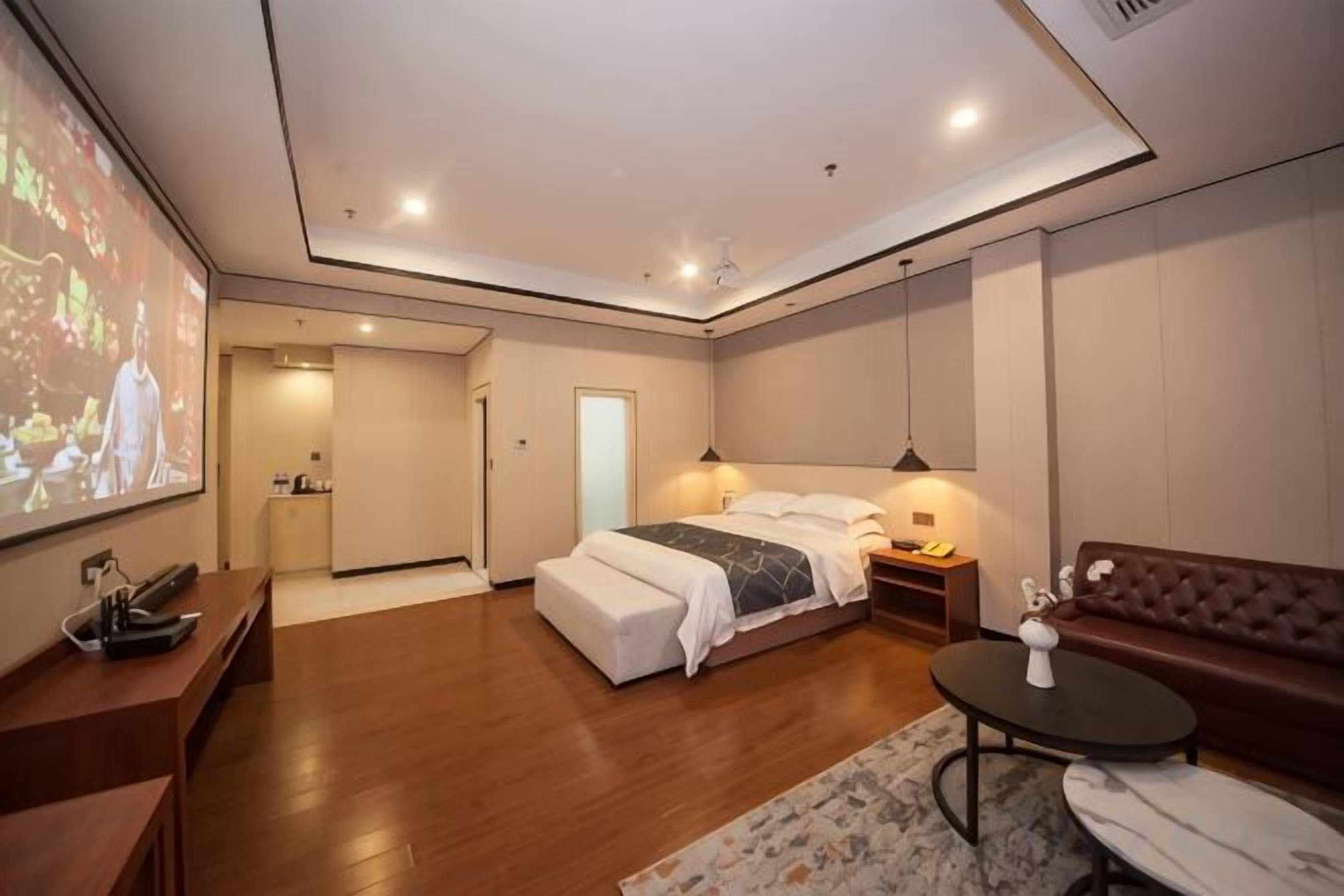 A modern bedroom with a bed, bedside tables, a seating area, and a television screen.