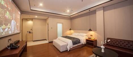 A modern bedroom with a bed, bedside tables, a seating area, and a television screen.