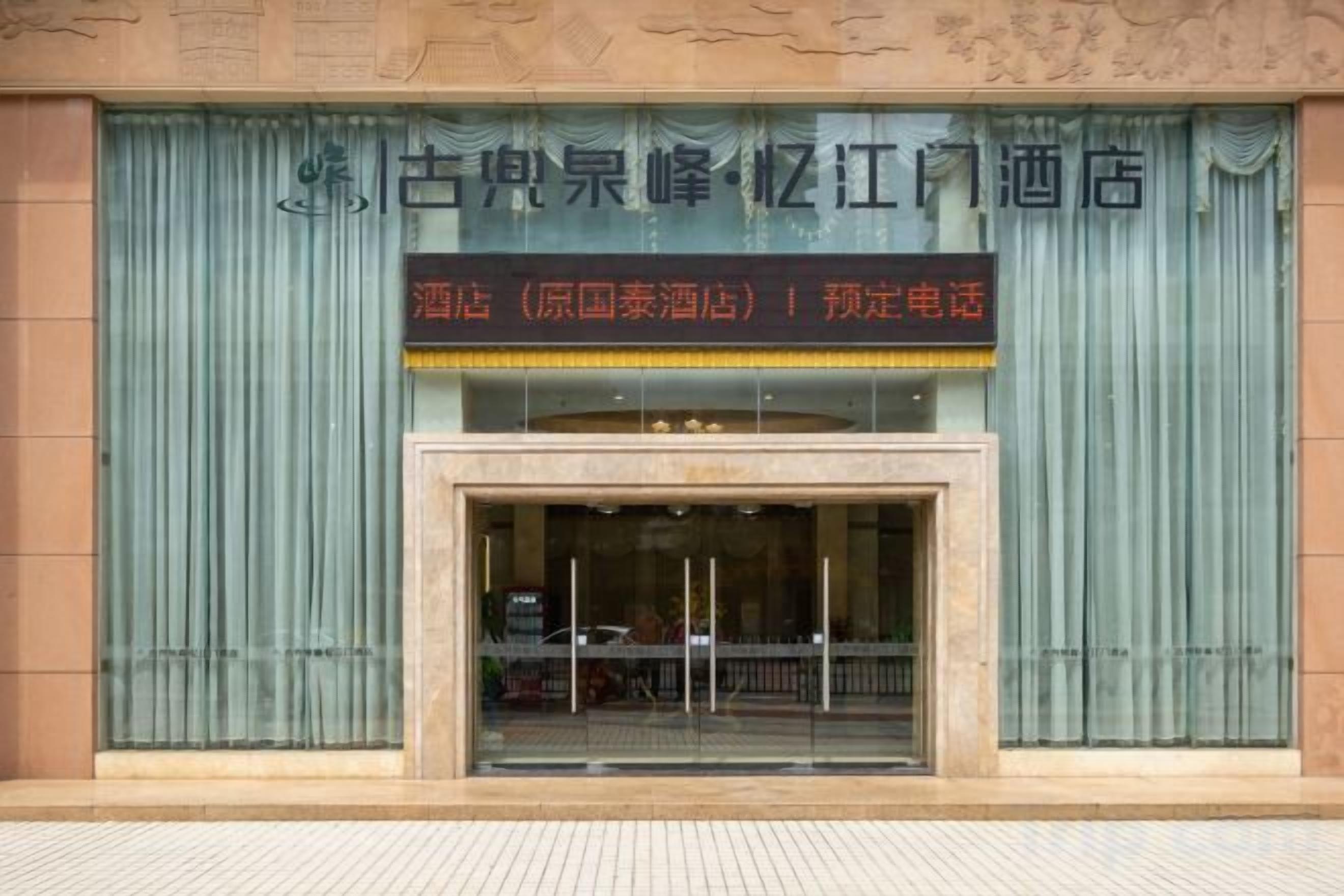 A hotel entrance with a large sign above the door, a glass entrance, and a tiled ground.