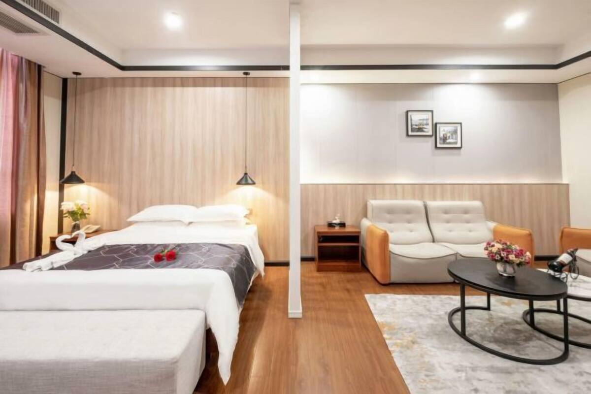 A hotel room with a bed, a sofa, a small table, and a wall-mounted TV.