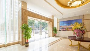A spacious lobby with a large glass door entrance, potted plants, and a decorative table with flowers. - Jiangmen Mintai Hotel (Jiangmen)