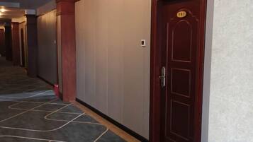 A hotel corridor with a wooden door, a number plaque, and a carpeted floor.