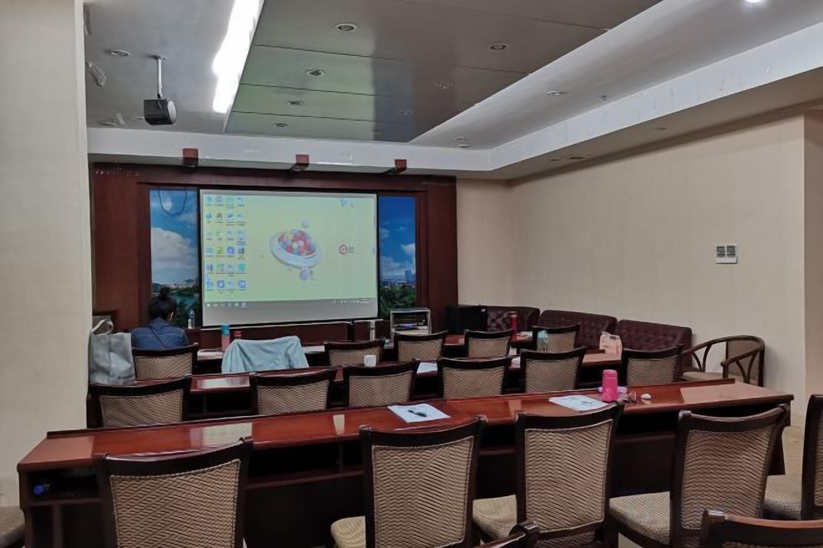 A conference room with a large screen, multiple tables, and chairs arranged for presentations.