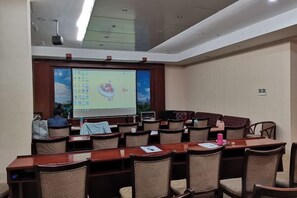 A conference room with a large screen, multiple tables, and chairs arranged for presentations. - Jiangmen Mintai Hotel (Jiangmen)
