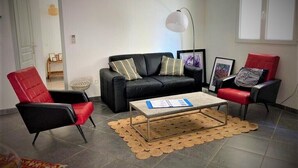 En stue med en sort sofa, røde lænestole, et sofabord i glas og en gulvlampe.