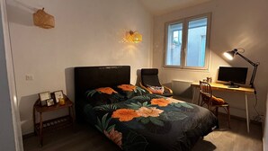 Et soveværelse med seng, skrivebord, stol, lampe og et vindue.