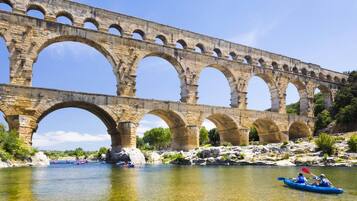 A stone bridge with multiple arches over a river, kayaks on the water, and greenery around.