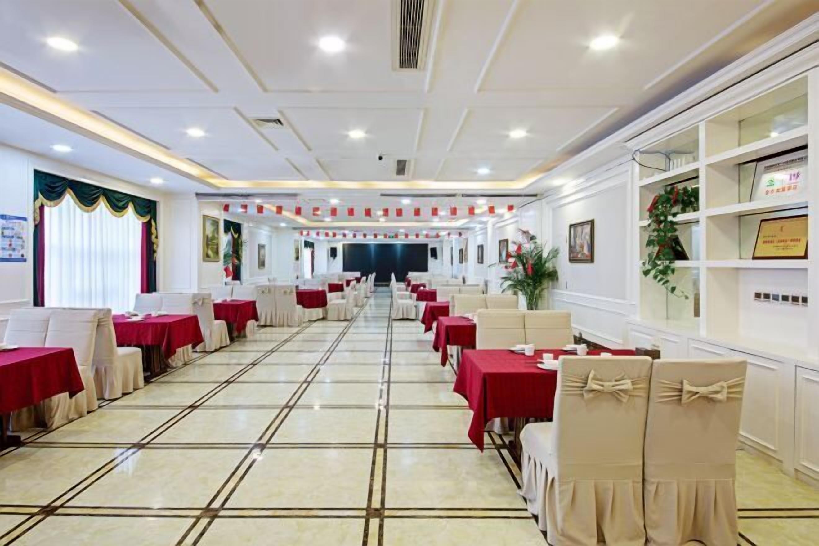 A banquet hall with rows of tables and chairs, a stage at the front, and framed certificates on the walls.