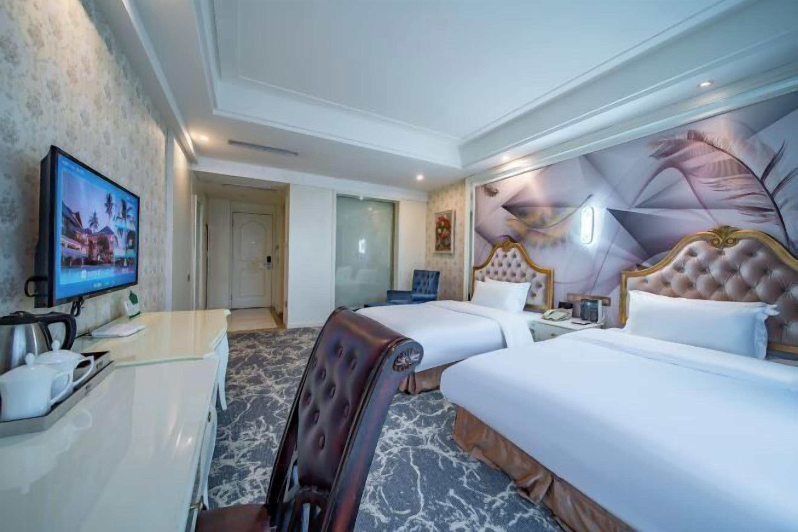 Quarto de hotel com duas camas, uma escrivaninha com televisão e uma parede decorativa.