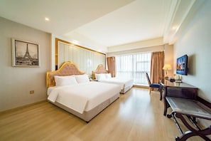 A hotel room with two beds, a desk, a chair, a TV, and a large window.