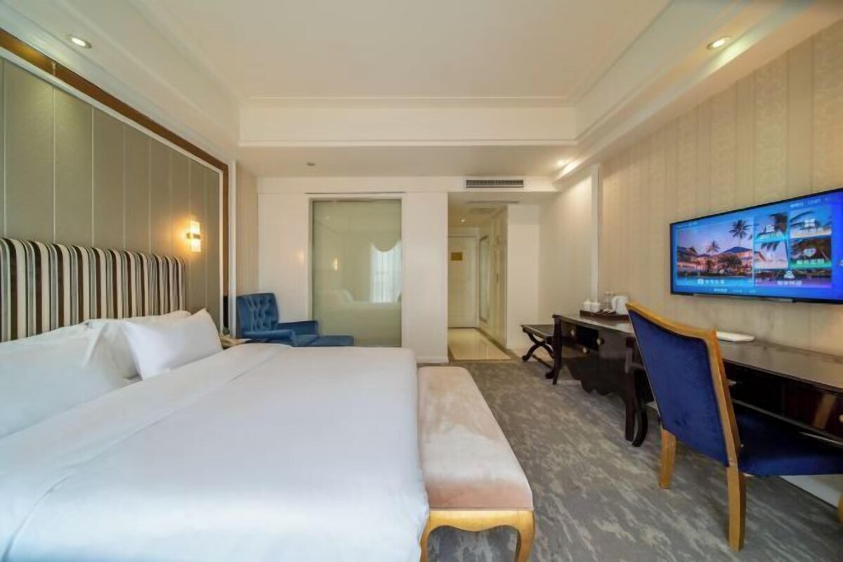 A hotel room with a large bed, a desk, a television, and a chair.