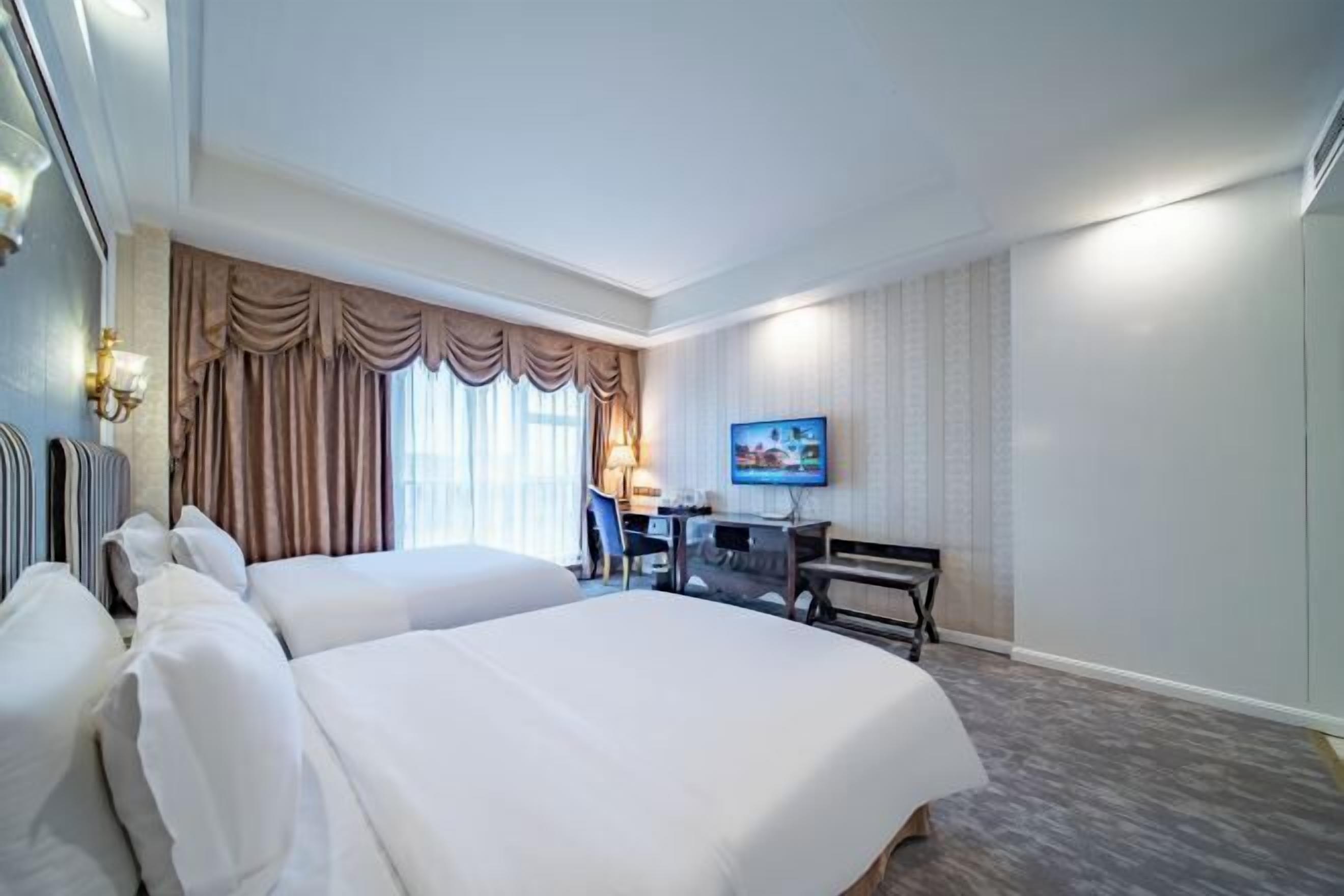 Habitación de hotel con dos camas, un escritorio, una silla, un televisor y una ventana con cortinas.