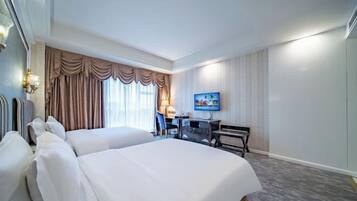 Habitación de hotel con dos camas, un escritorio, una silla, un televisor y una ventana con cortinas.