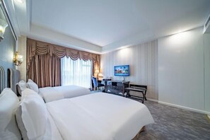 A hotel room with two beds, a desk, a chair, a television, and a window with curtains.