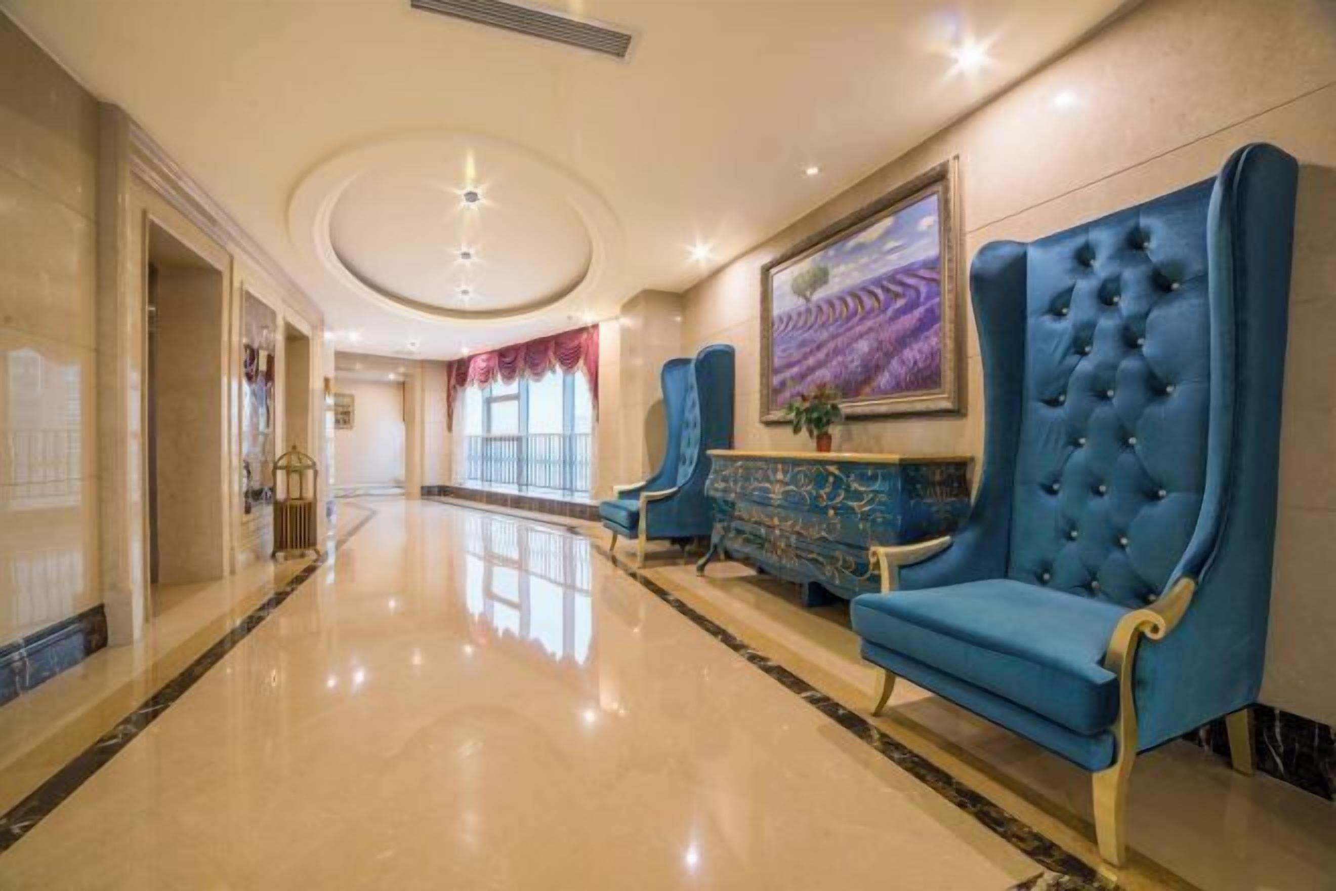 A hotel lobby with a polished marble floor, blue upholstered chairs, and a large painting on the wall.