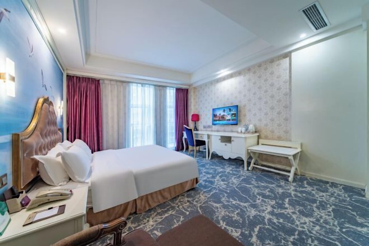 A hotel room with a large bed, a desk, a chair, and a small table.