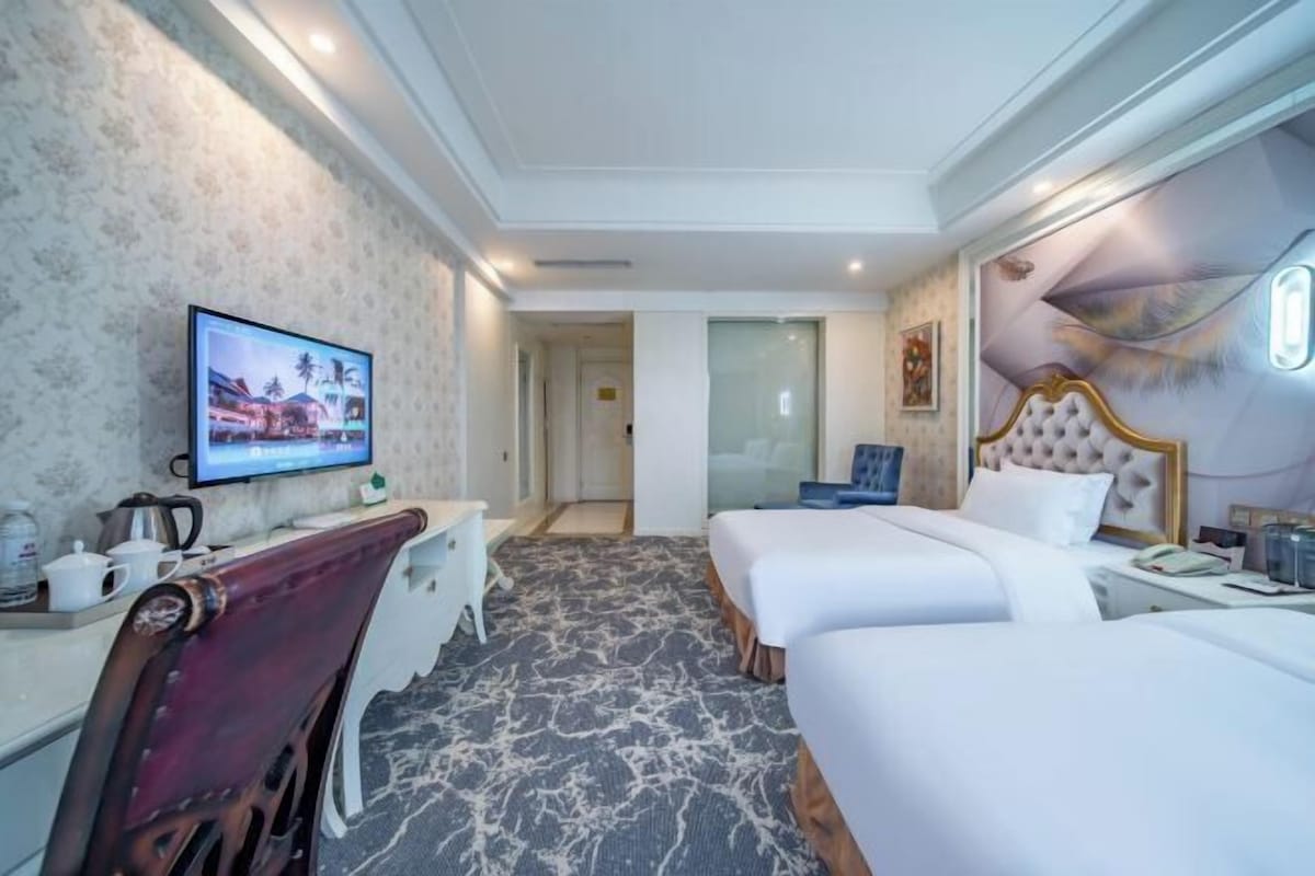 A hotel room with a TV, two beds, a desk, and a chair.
