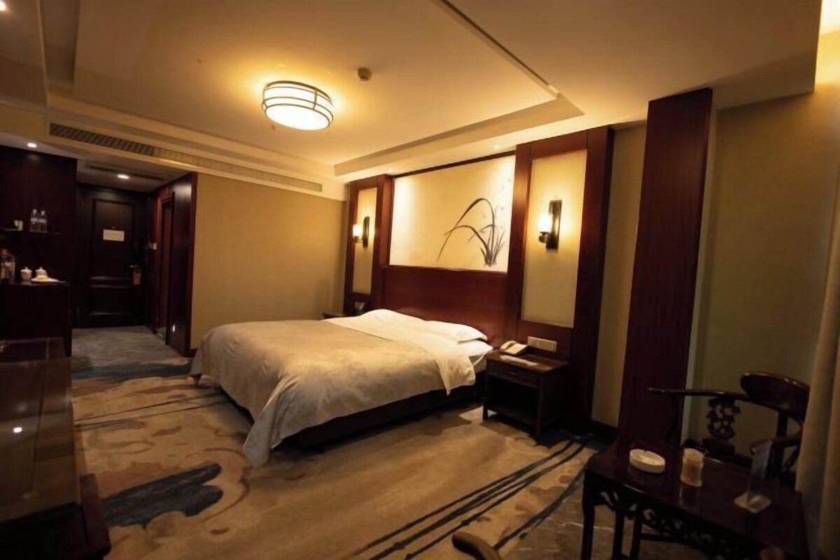 A hotel room with a large bed, a bedside table, a nightstand, a lamp, and a wall-mounted artwork.