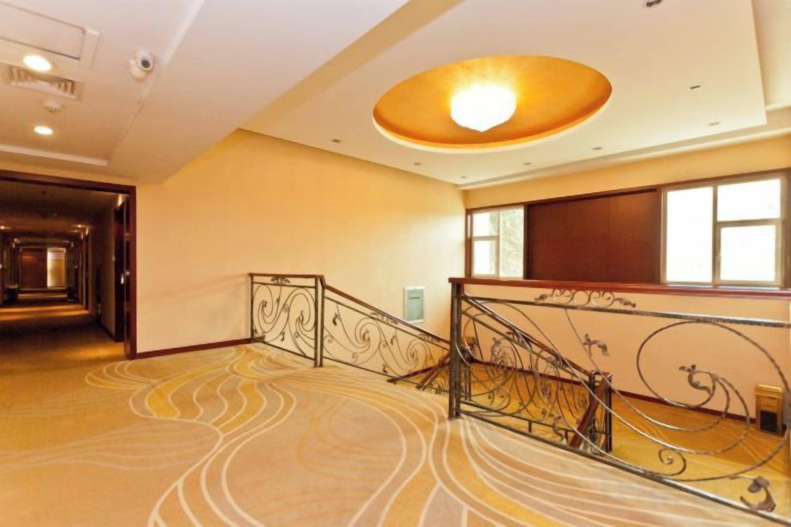 Un vestíbulo de hotel con una escalera monumental, una alfombra estampada y un ventanal amplio.