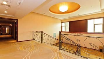 Un vestíbulo de hotel con una escalera monumental, una alfombra estampada y un ventanal amplio.