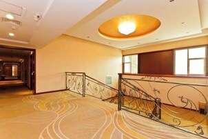 Un vestíbulo de hotel con una escalera monumental, una alfombra estampada y un ventanal amplio.