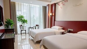 Ein Hotelzimmer mit zwei Betten, einem Schreibtisch, einem Stuhl, einem Fernseher und einem Fenster mit Vorhängen.