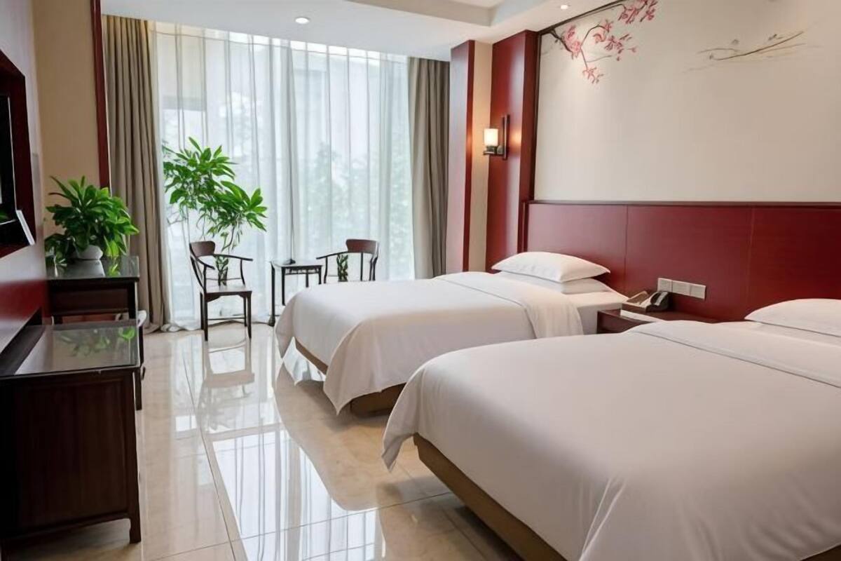 A hotel room with two beds, a desk, a chair, a TV, and a window with curtains.