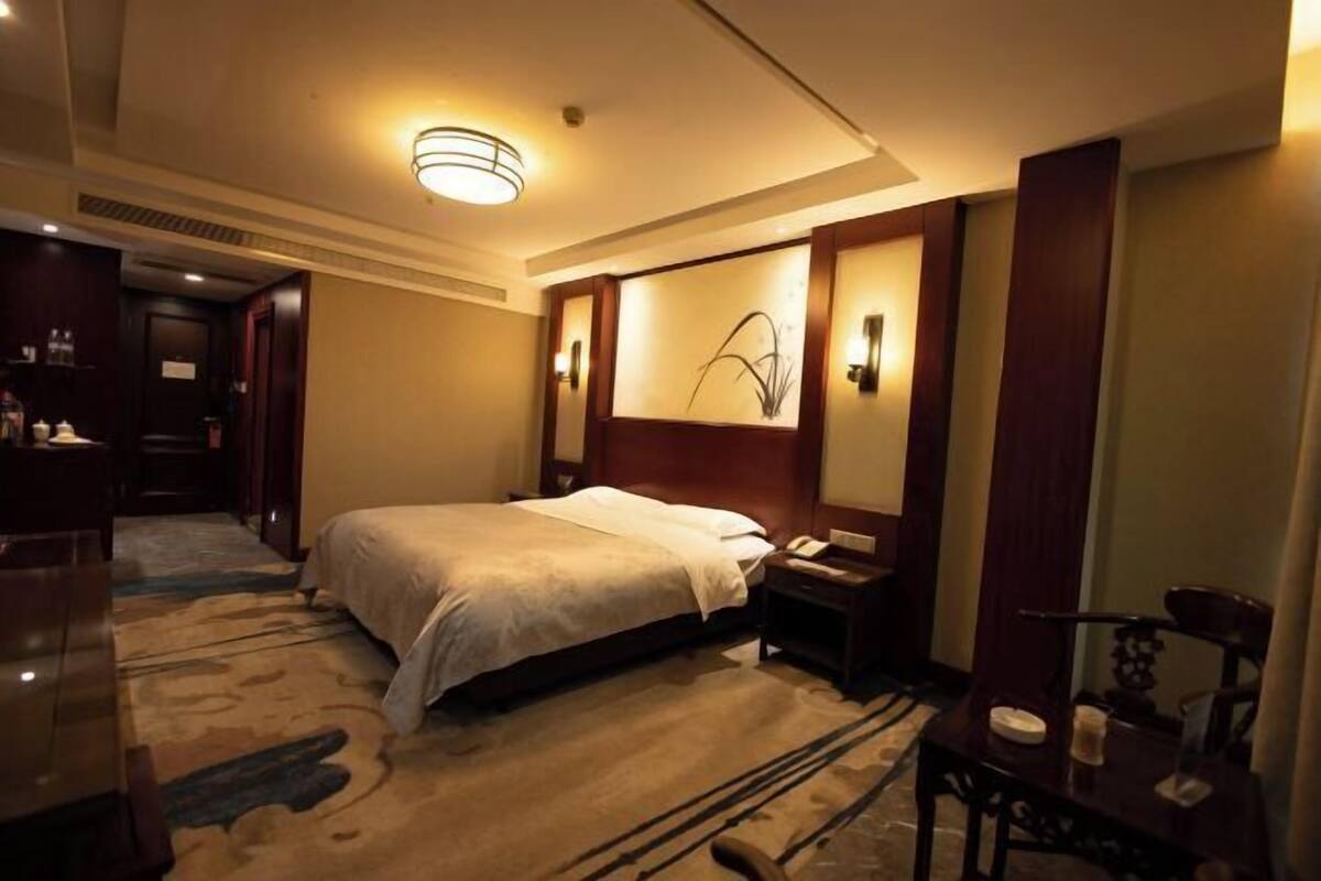 A hotel room with a bed, bedside table, lamp, and a painting on the wall.