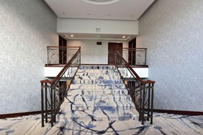 A hotel lobby with a carpeted staircase, a reception desk, and a wall-mounted light fixture. - Dongsheng Hotel (Zouping)