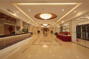 A hotel lobby with a reception desk, a chandelier, and a red carpeted area.