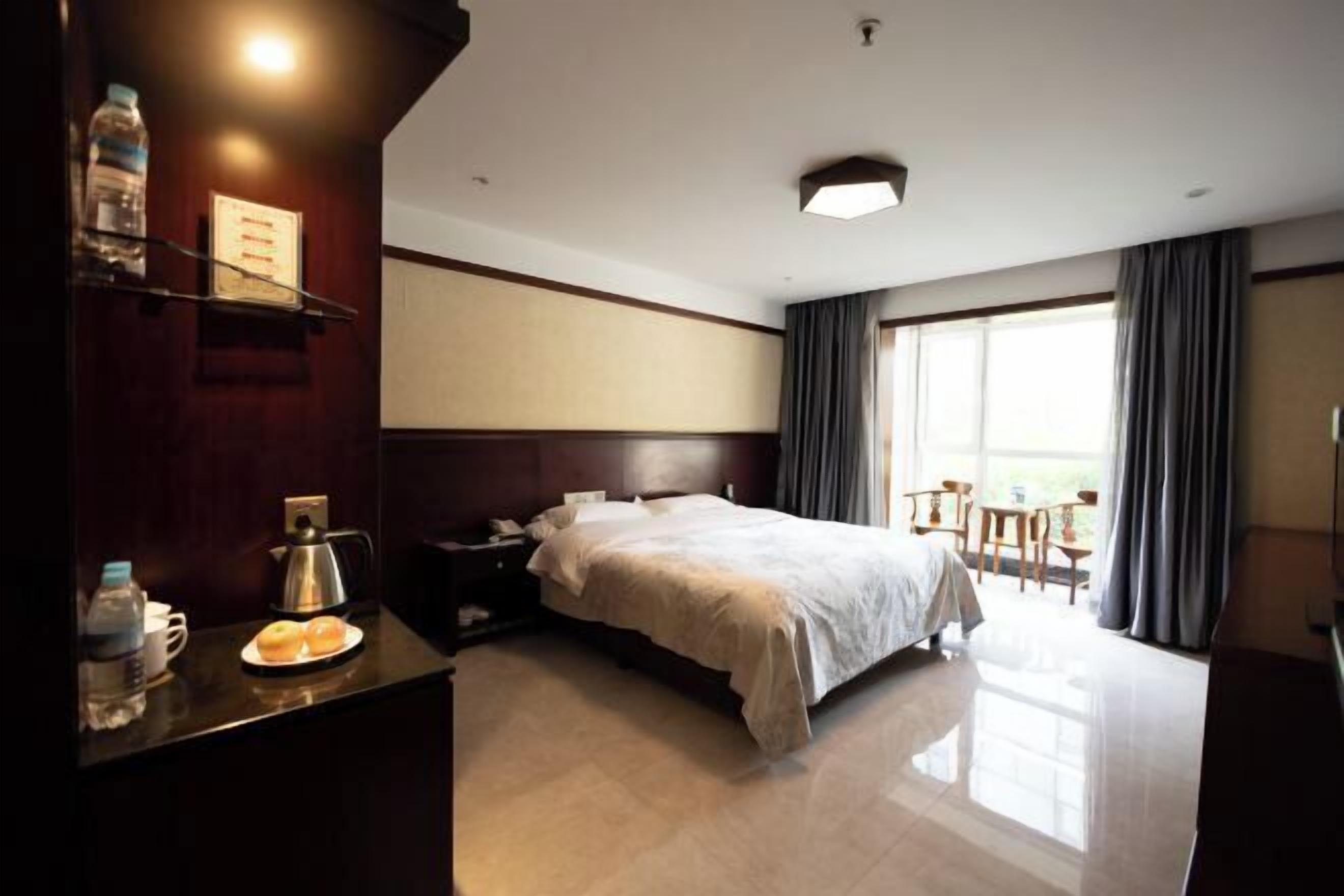 A hotel room with a bed, bedside table, and a view of the outdoors.