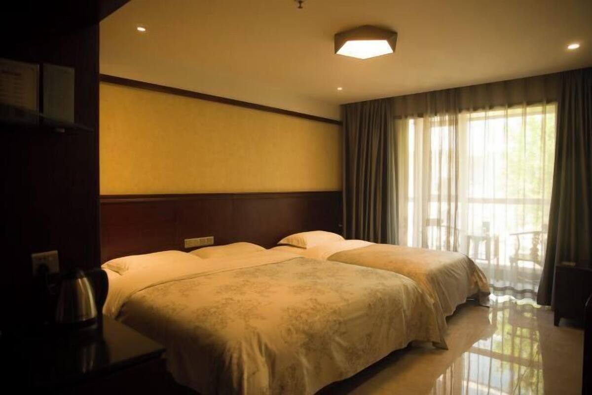 A hotel room with two beds, a nightstand, a lamp, and a window with curtains.