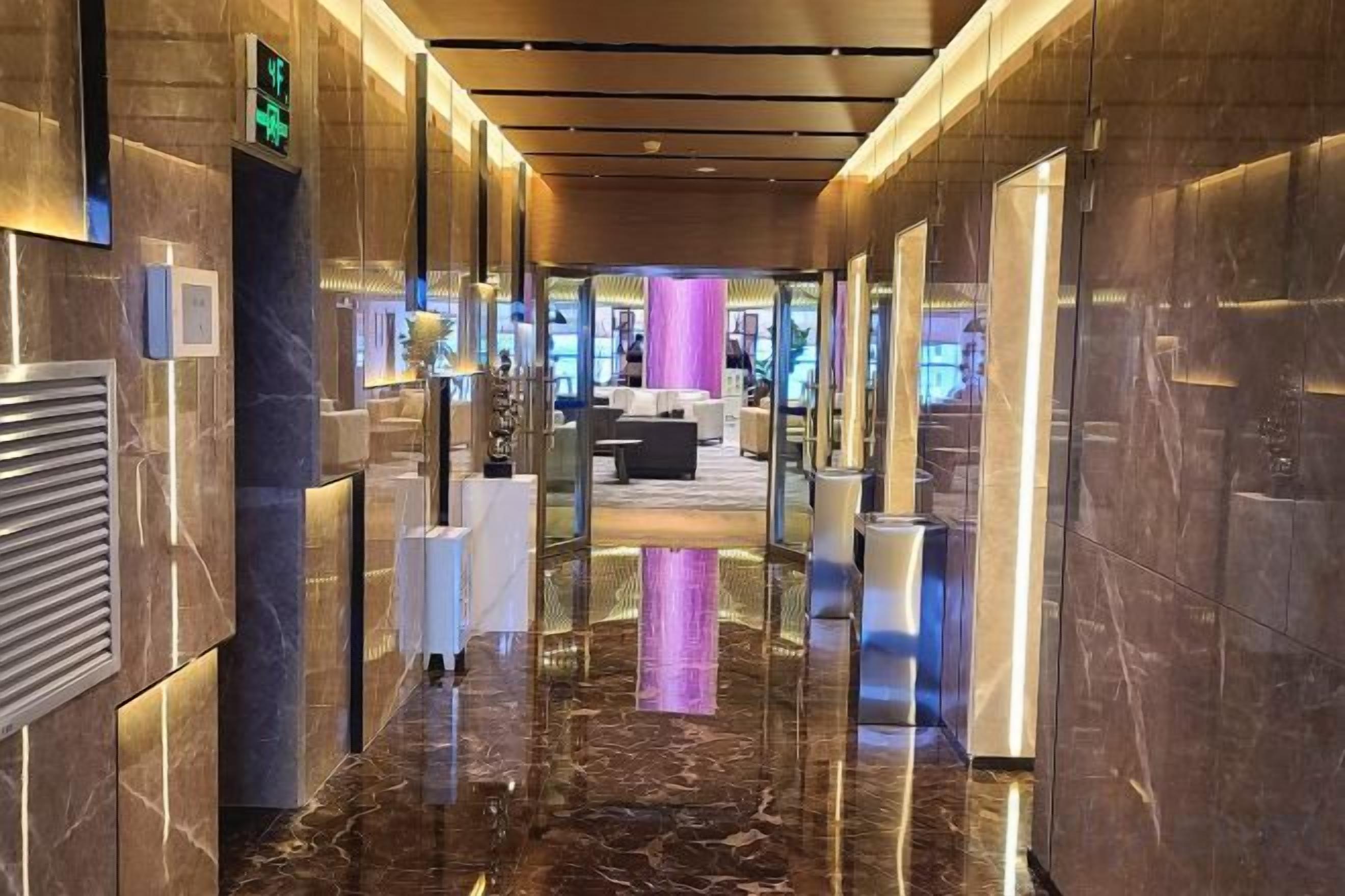 Un moderno vestíbulo de hotel con piso de mármol, un mostrador de recepción y un área de descanso al fondo.