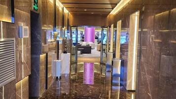 Un moderno vestíbulo de hotel con piso de mármol, un mostrador de recepción y un área de descanso al fondo.