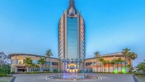 A modern hotel with a central tower, a fountain in front, and a landscaped area.
