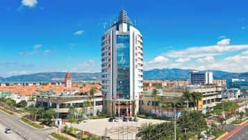 Un hotel moderno con una fachada curva distintiva, situado en una ciudad con cielo azul despejado y montañas al fondo.