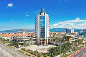 Un hotel moderno con una fachada curva distintiva, situado en una ciudad con cielo azul despejado y montañas al fondo.