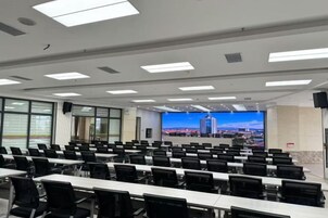 A conference room with rows of tables and chairs, a large screen, and a cityscape view.