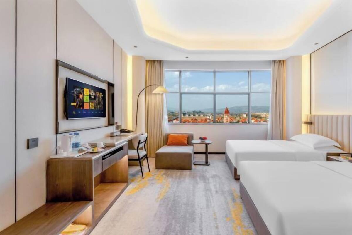Habitación de hotel con escritorio, dos camas, televisión y vista a un paisaje urbano.