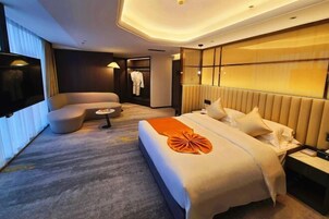 Una habitación de hotel moderna con una cama grande, un sofá, una mesita y un televisor.
