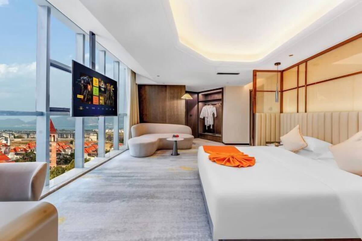 Una habitación de hotel moderna con un ventanal grande, un sofá, una cama y un televisor.