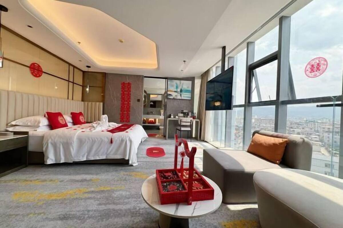 Una habitación de hotel moderna con cama, sofá, zona de comedor y un amplio ventanal con vistas a la ciudad.