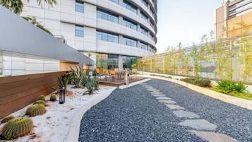 A modern building with a curved facade, outdoor seating area, and a gravel pathway.