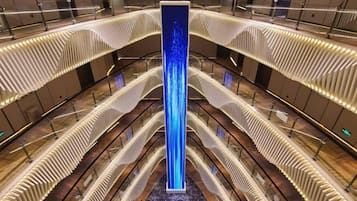 Een moderne atrium met een centrale verticale lichtinstallatie, meerdere balkons en een vloer met een patroon.
