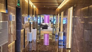 A modern hotel corridor with marble floors, glass doors, and a central seating area with a purple backdrop.
