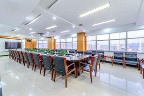 Een vergaderzaal met een lange tafel, stoelen en een stadsgezicht door grote ramen.