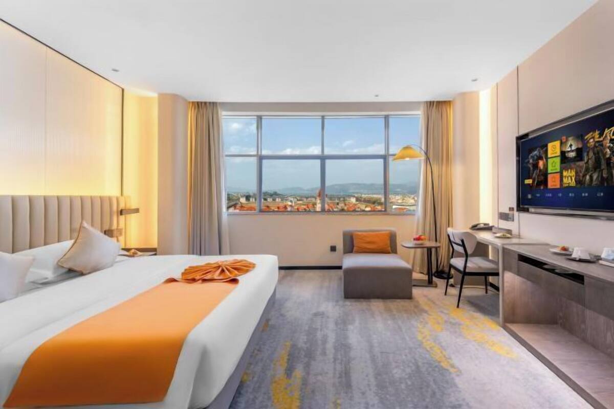Habitación de hotel con cama, escritorio, silla, una mesita pequeña y un ventanal con vistas.